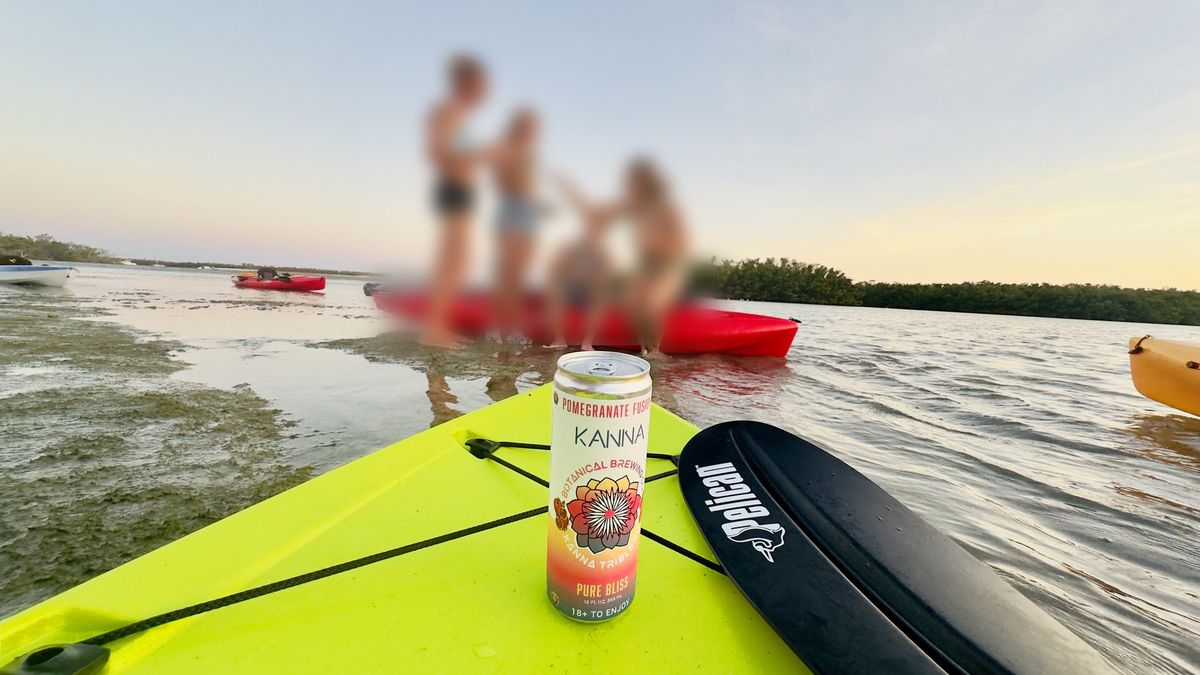 A can of Kanna Pomegranate Fusion on a kayak at a sandbar, friends in the background